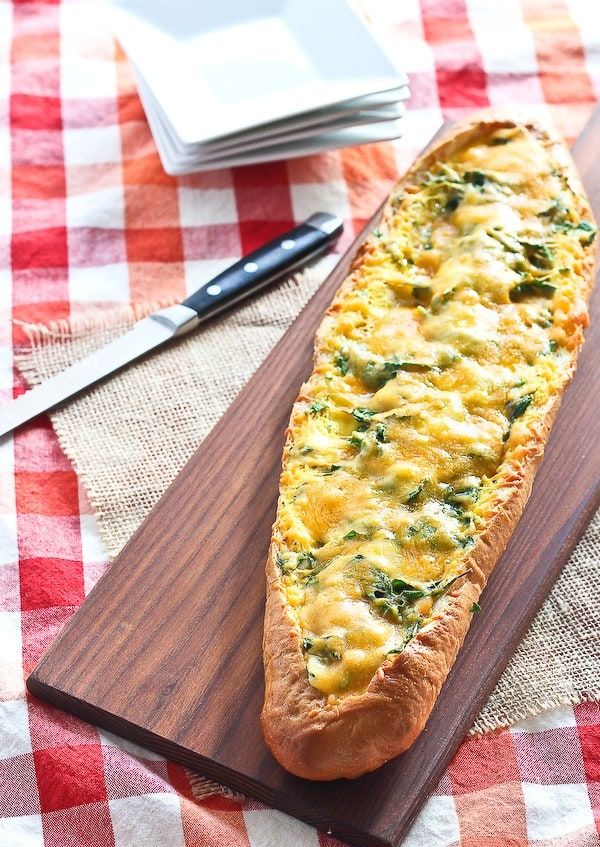 bread with cheese and spinach is on a wooden cutting board next to a knife