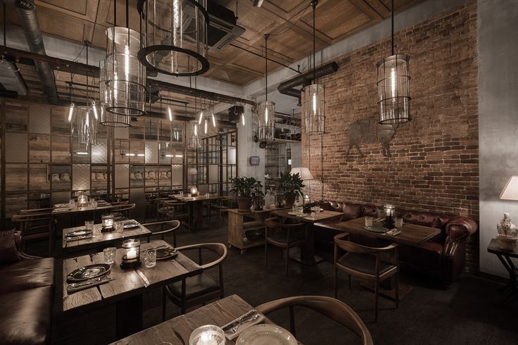 the interior of a restaurant with wooden tables and brown leather chairs, exposed brick walls and hanging lights