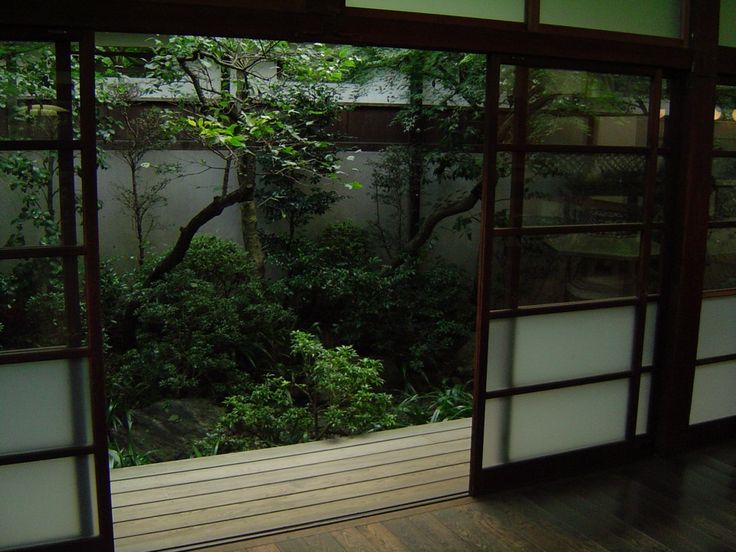 an open room with sliding glass doors leading to a tree filled garden in the background