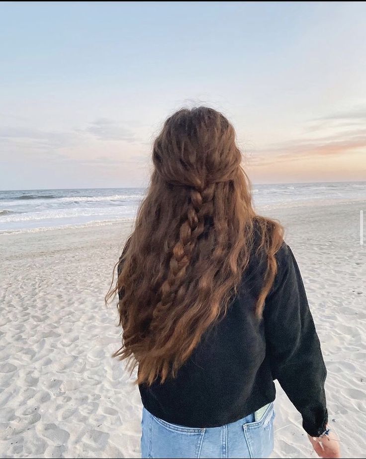 a woman standing on top of a sandy beach next to the ocean with long hair