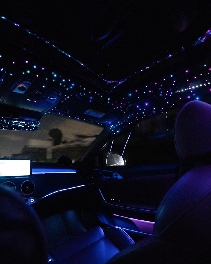 the interior of a car with blue and purple lights shining on the ceiling, along with black leather seats