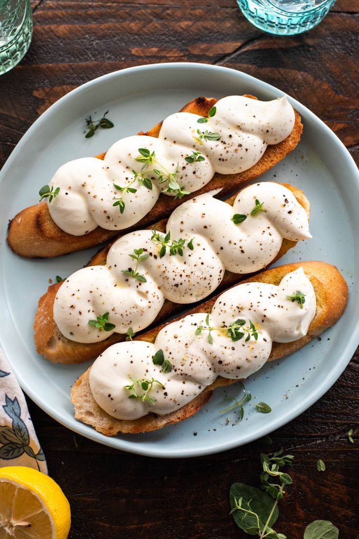 bread topped with white sauce and herbs on a plate next to sliced lemon wedges