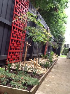 an outdoor garden area with red and black fenced in plants, trees and shrubs