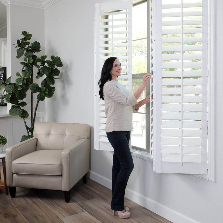 a woman opening the blinds in her living room