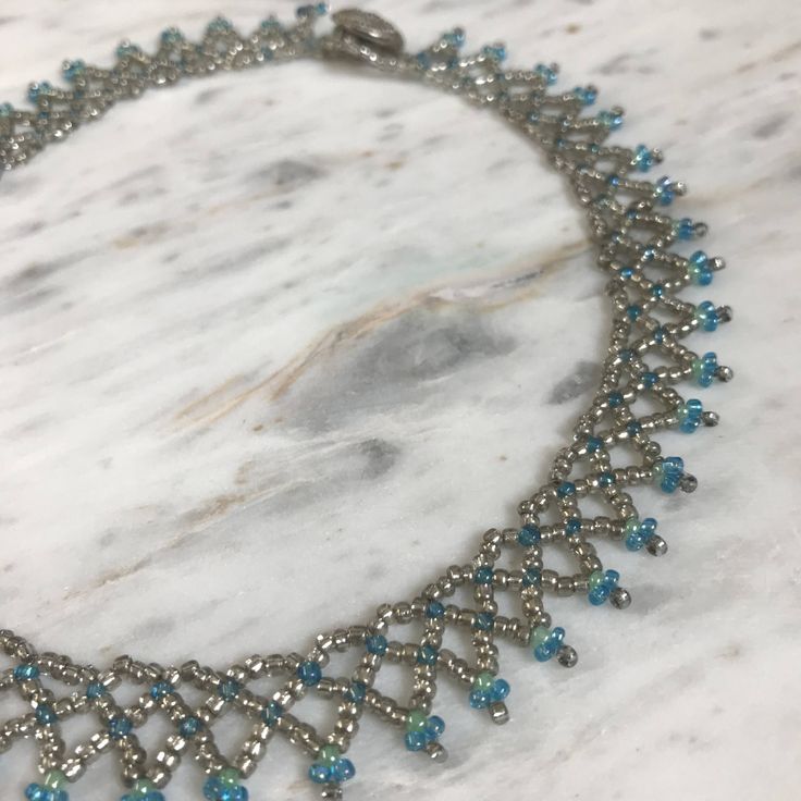 This beautiful seed bead choker was handmade by a friend and is perfect for everyday wear.  It features clear silver beads with blue and green accent beads.  the closure is a plastic silver button that slips though a loop on the other side.  From end bead to loop it measures 41 cm. If you are not sure if it will fit try using a string or ribbon around your neck to measure. Turquoise Beaded Choker With Round Beads, Blue Beaded Chain Choker, Handmade Silver Beaded Choker Necklace, Blue Beads With Bead Caps For Jewelry Making, Adjustable Blue Beaded Necklaces With Bead Caps, Adjustable Silver Choker With Colorful Beads, Silver Adjustable Choker With Colorful Beads, Adjustable Silver Choker With Spacer Beads, Silver Choker With Colorful Beads, Adjustable