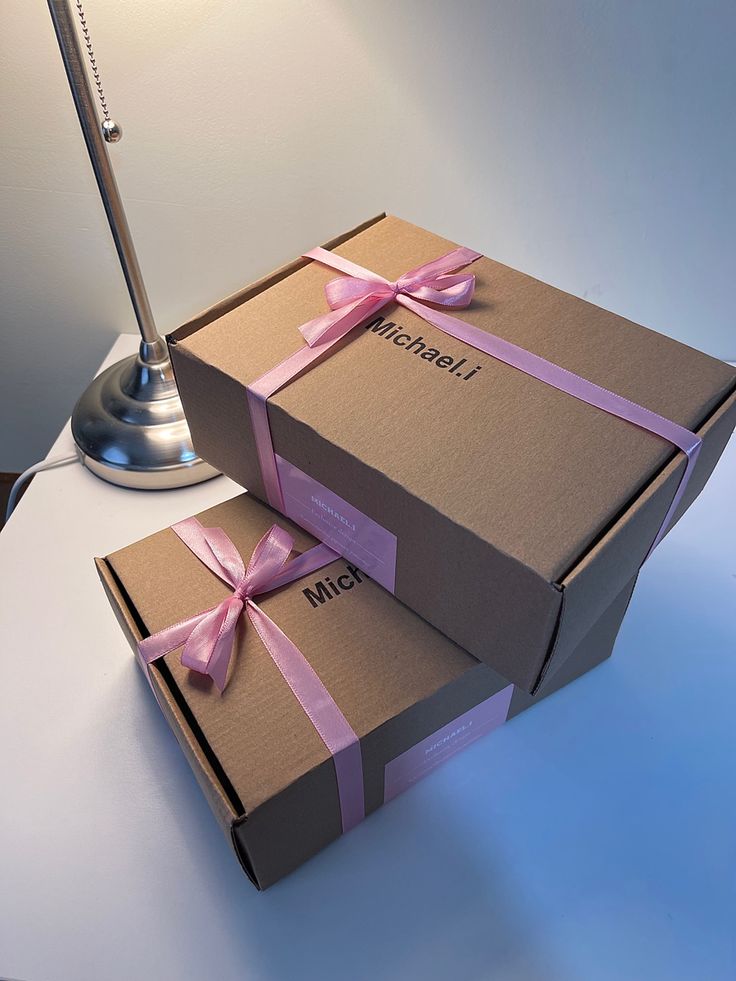 two brown boxes with pink bows on them are sitting next to a lamp that is turned on