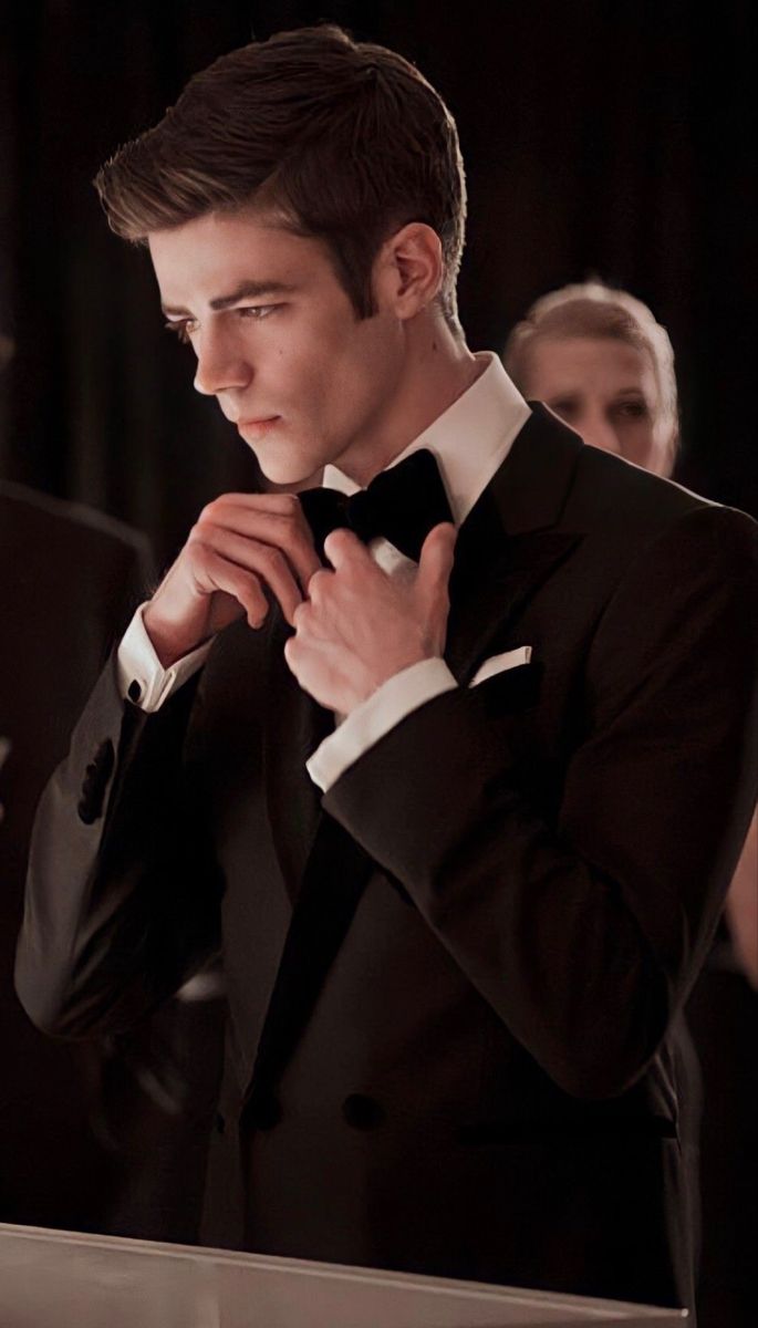 a man in a tuxedo adjusts his bow tie as others look on