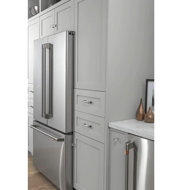 a stainless steel refrigerator and freezer combo in a kitchen with white cabinets, marble counter tops and wood flooring