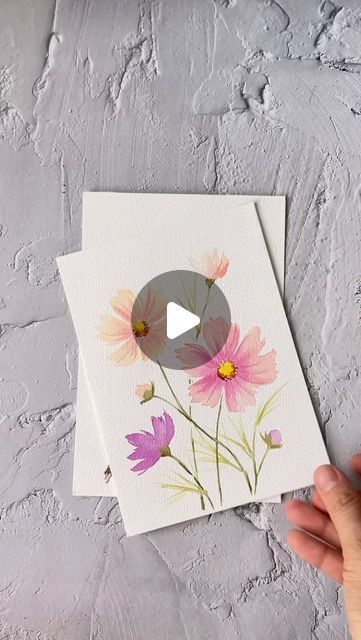 someone is holding up some cards with flowers on them, and the card has a video playing button