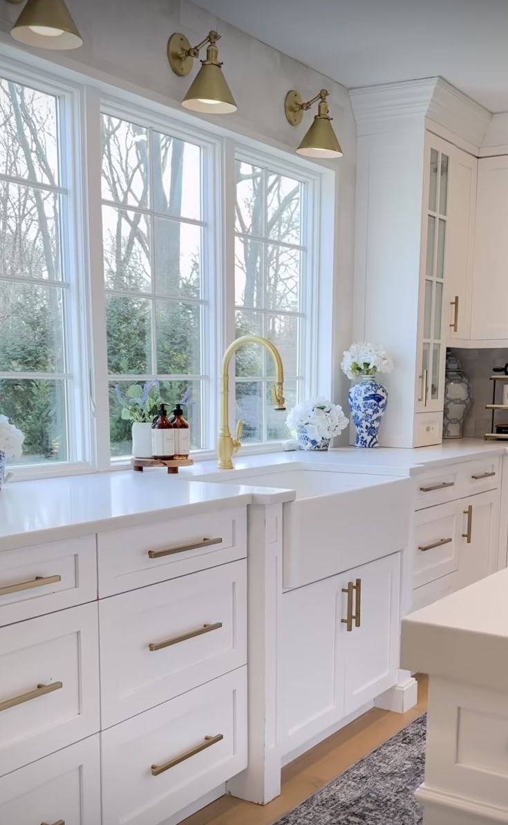 a large kitchen with white cabinets and gold hardware on the countertops, along with two windows