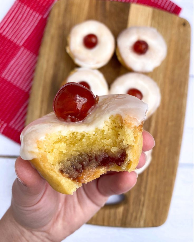 a hand holding a half eaten cherry filled donut with icing and cherries