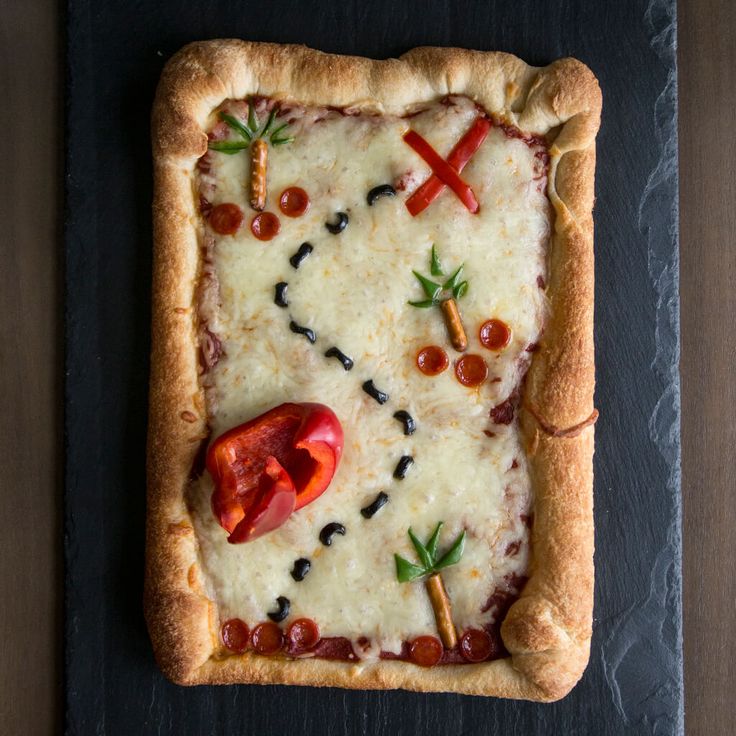 a square pizza with cheese and tomatoes on it sitting on a black slate platter