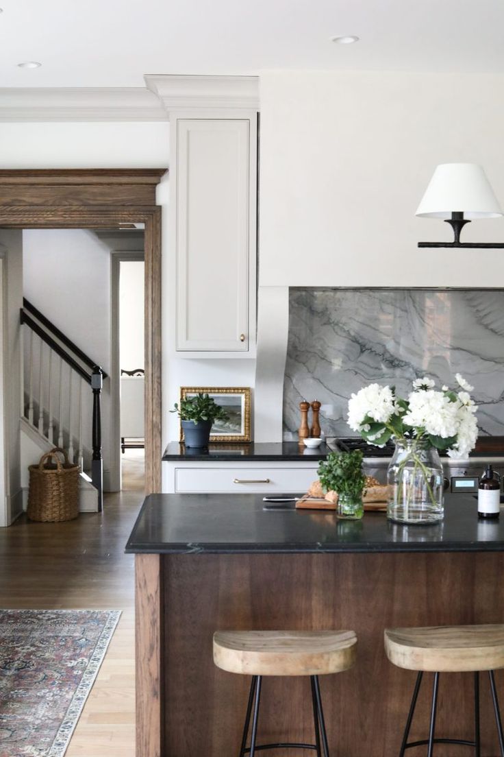 a kitchen with marble counter tops and wooden stools in front of an island that has flowers on it