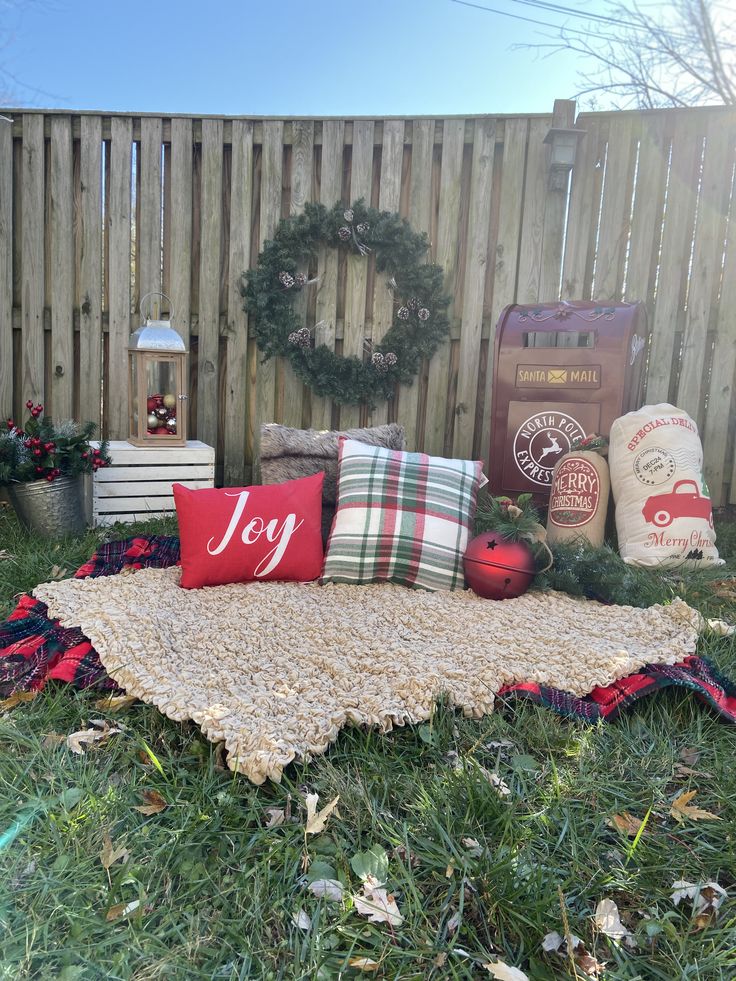 a blanket, pillows and wreaths are on the grass in front of a fence