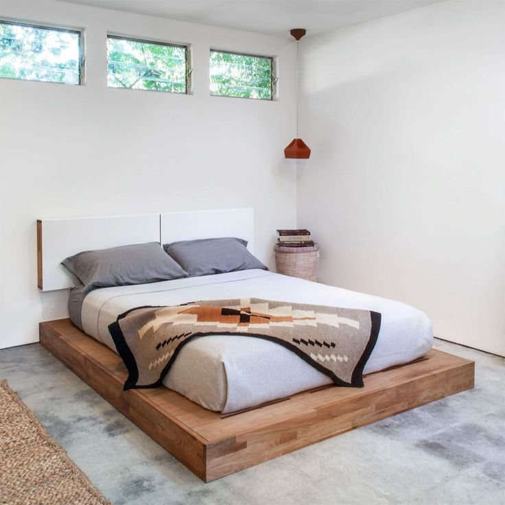 a bedroom with a bed, rugs and windows in the room that has white walls