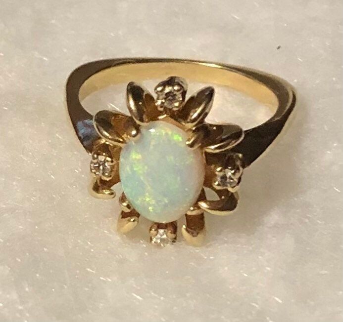 This fabulous mid century ring is 14 karat yellow gold with a lustrous oval cabochon cut opal with a little halo accented with 4 tiny diamonds, creating a wonderful classic design. The opal is close to 10mm by 7mm approximately and has a lovely iridescence. While I am not a gemologist, this appears to be a nice high-quality opal with tons of fire and brilliance and beautiful hues of green and blue and pink. The ring dates to the 1960s-70s, and it weighs about 5.5 grams, And it's approximately a Oval Opal Ring In Yellow Gold Stamped 14k, Heirloom Oval Opal Ring Collectible, Hallmarked Oval Diamond Opal Ring, Classic Oval Opal Ring Collectible, Vintage Oval Opal Ring For Formal Occasions, Vintage Oval Opal Ring For Formal Events, Vintage 14k Gold Oval Cabochon Opal Ring, Collectible Yellow Gold Opal Ring Oval Cabochon, Collectible Oval Cabochon Opal Ring In Yellow Gold