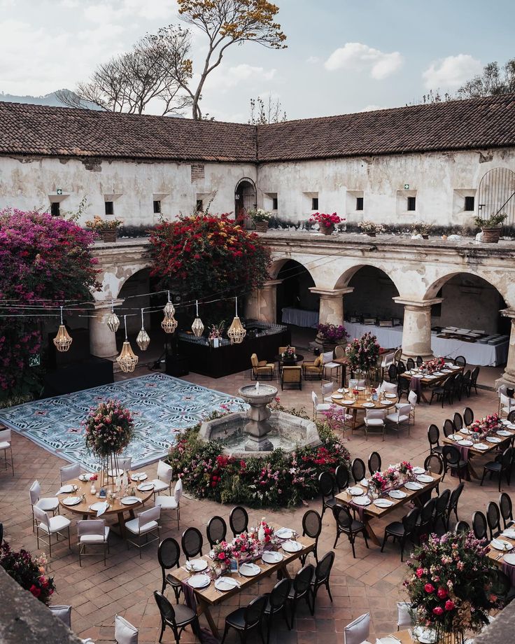 an outdoor dining area with tables, chairs and flowers on the table in the center