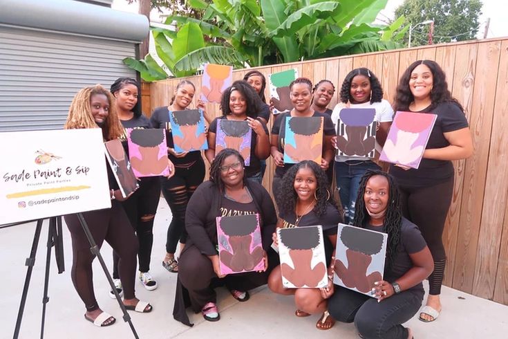 a group of women standing next to each other holding up paintings in front of a fence