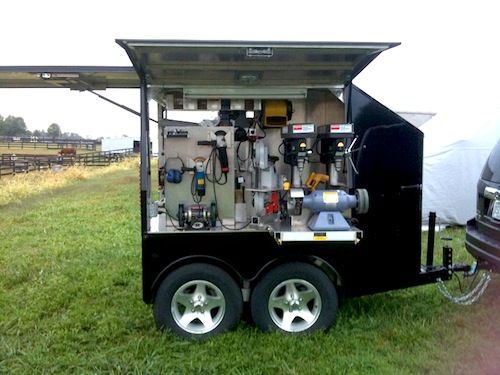 the back end of a black truck with tools in it's trailer parked on grass