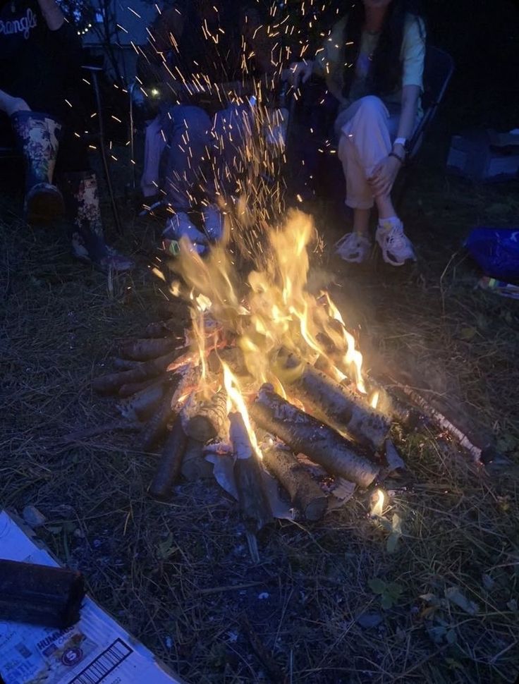 people sitting around a campfire with lots of sparks coming out of the fire pit