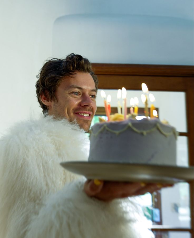 a man in a fur coat holding a cake with lit candles on it and looking at the camera