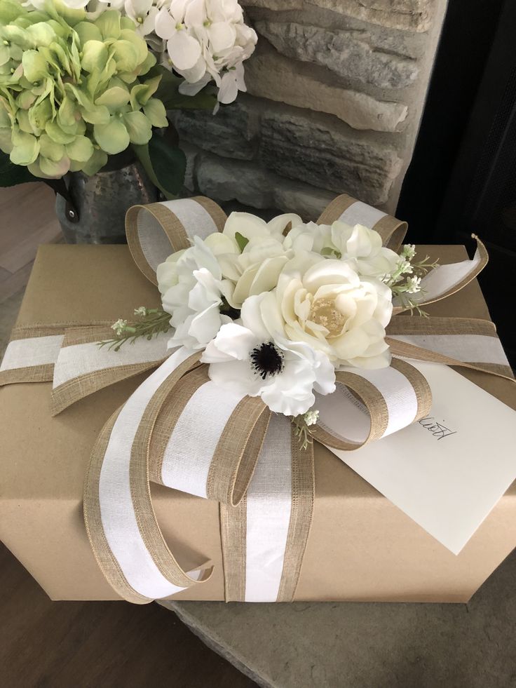 a gift wrapped in brown paper with white flowers on top and a card tied to it