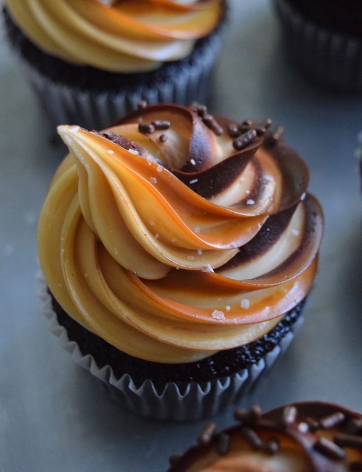 several cupcakes with chocolate frosting and caramel swirl on top, sitting on a table