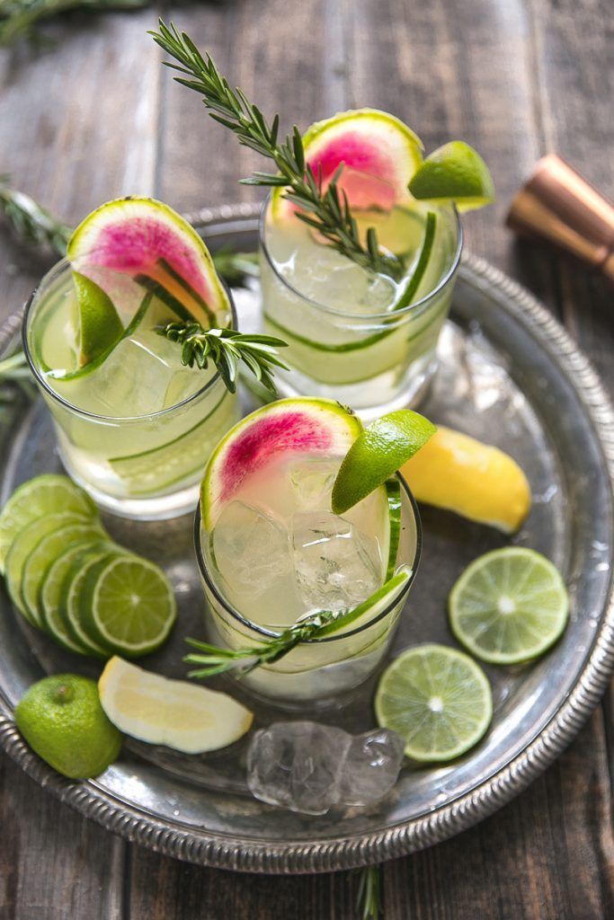 three glasses filled with watermelon and limeade on a silver plate next to lemon wedges