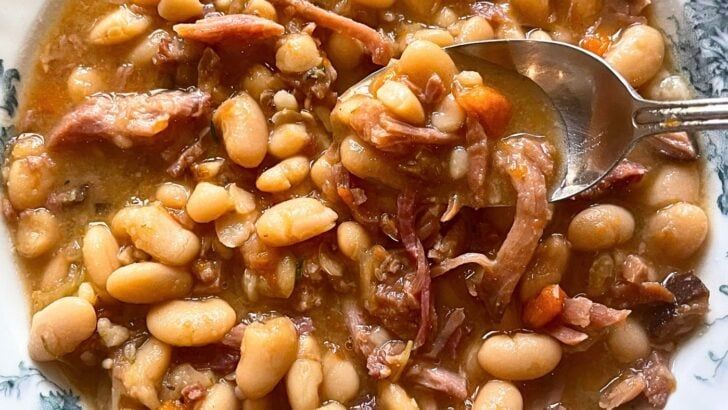 a white bowl filled with beans and meat on top of a blue and white plate