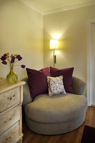 a living room with a round couch next to a dresser and lamp on the wall