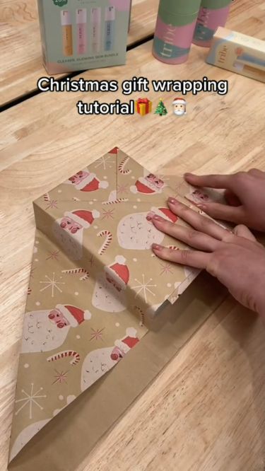 someone is wrapping up a gift box on the table with christmas wrapping around it's edges