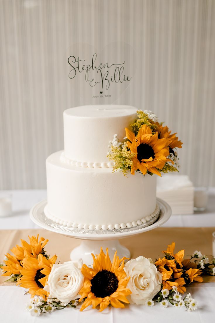 a white wedding cake with sunflowers on top