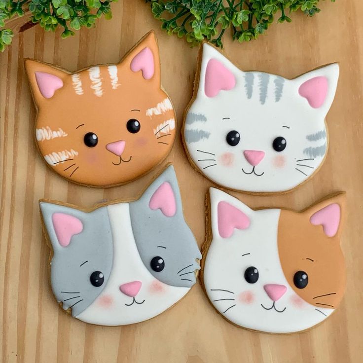 four decorated cat cookies sitting on top of a wooden table