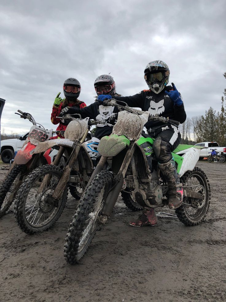 three people sitting on dirt bikes in the mud