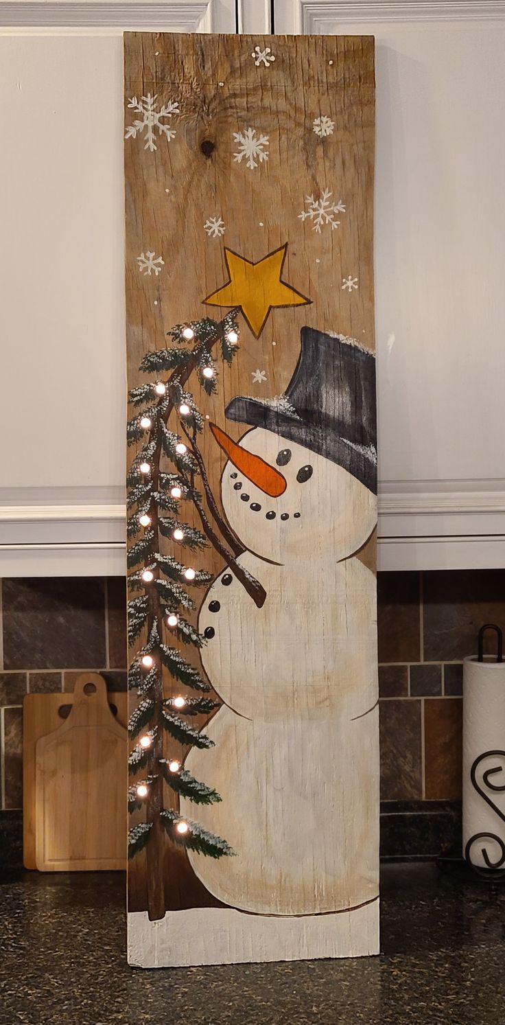 a wooden sign with a snowman holding a christmas tree on it's side