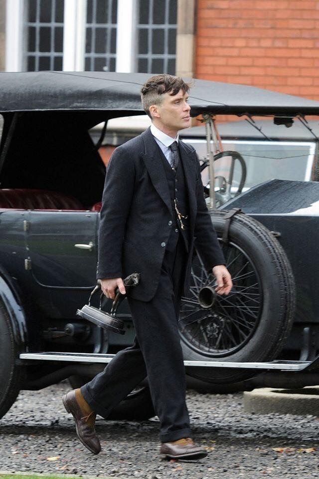 a man in a suit walking past an old car