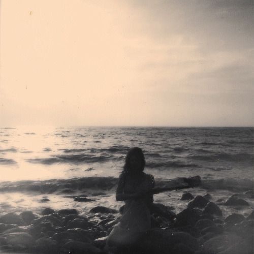 a woman sitting on rocks near the ocean