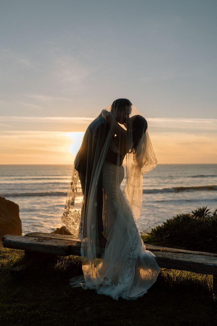 a bride and groom kissing in front of the ocean at their sunset wedding photo shoot