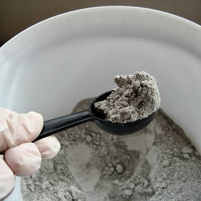 a person in white gloves holding a black spoon with some gray powder on top of it