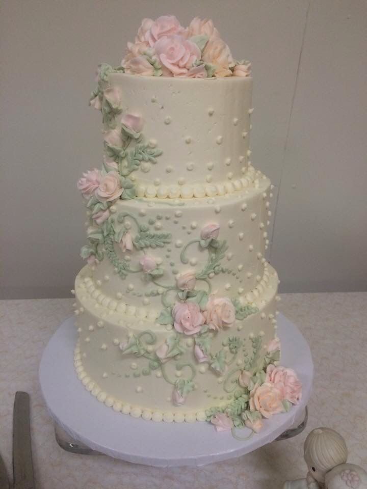 a three tiered wedding cake with pink flowers and pearls on the top, sitting on a table next to silverware