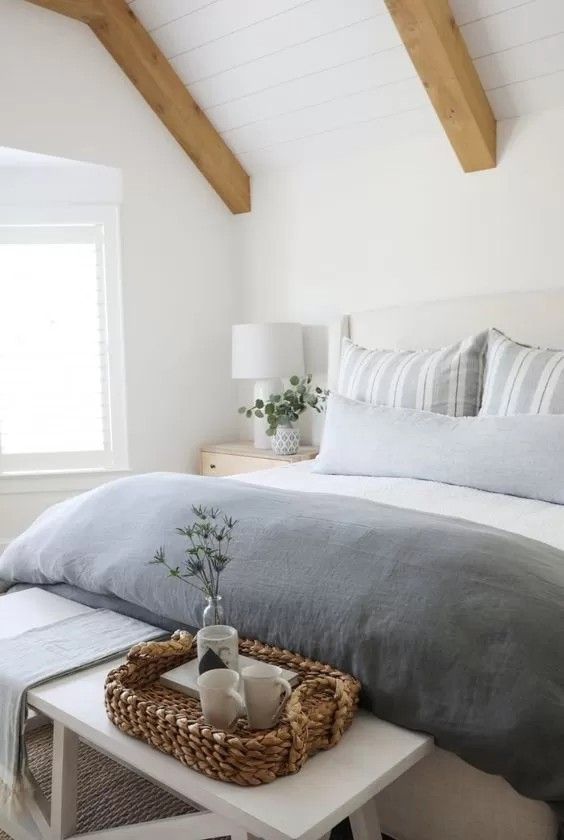 a bedroom with white walls and wooden beams on the ceiling, along with a large bed covered in gray linens