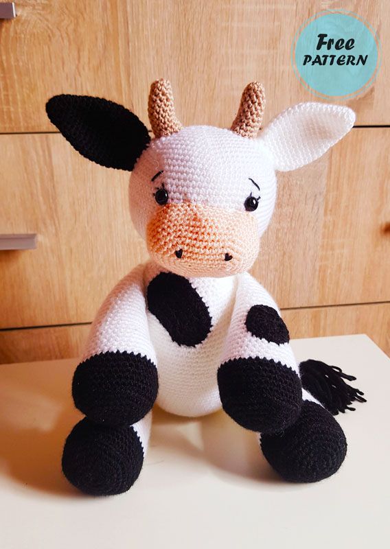 a knitted cow sitting on top of a table next to a wooden cabinet door