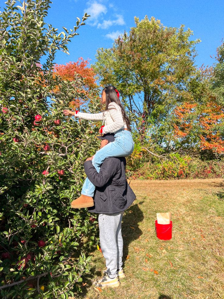 a woman and child picking apples from an apple tree in the fall with red buckets