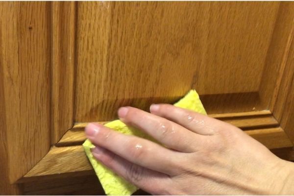 a person wiping up with a cloth on the handle of a wooden cabinet door knob