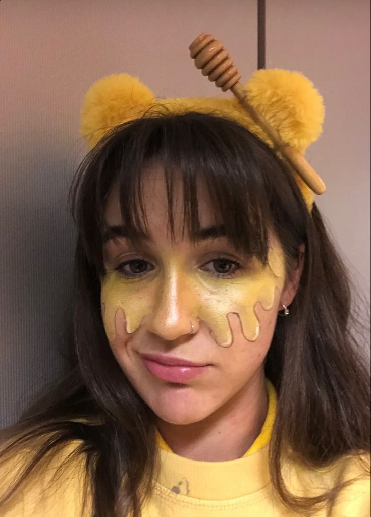 a woman with yellow paint on her face wearing a bear ears and honey comb hat