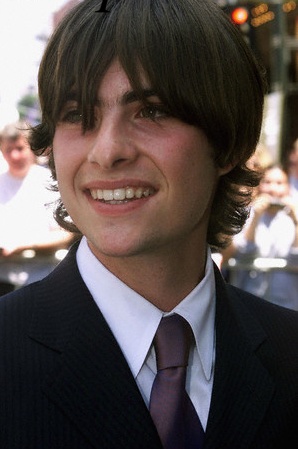 a young man in a suit and tie smiling at the camera with people behind him