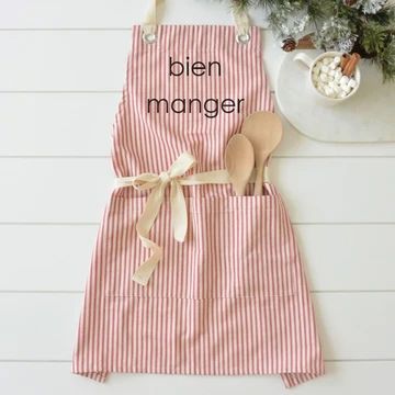 a pink and white striped apron with wooden spoons on it next to a potted plant