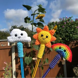 three crocheted sunflowers with faces on them in front of a fence