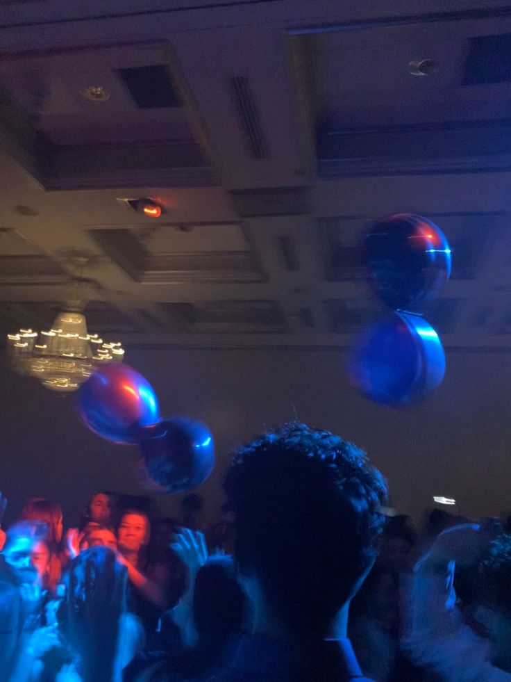 a group of people standing in front of a crowd at a party with blue and red balloons