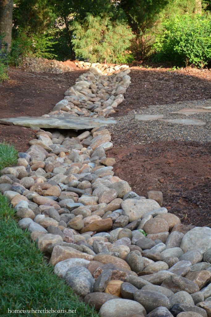 a stone path made out of rocks in the middle of a field with trees and bushes behind it